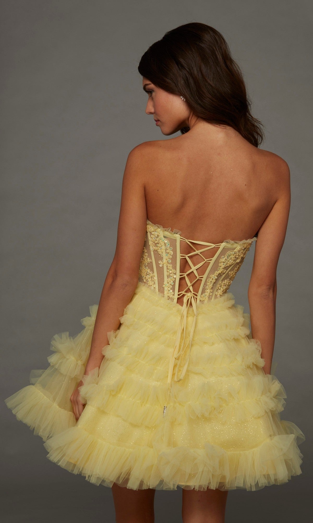 A woman models the Short Homecoming Dress: Alyce 30094, showcasing its strapless lace corset bodice and layered tulle skirt against a plain background.